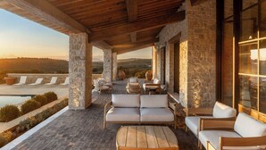 A covered outdoor seating area with stone pillars, a wooden ceiling, and a view of the landscape.