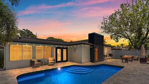 Et moderne hus med swimmingpool, udendørs møbler og en solnedgangshimmel.