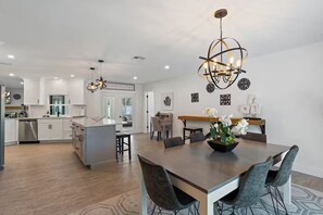 A modern kitchen with white cabinets, a central island, and a dining area with a wooden table and chairs. - Sarasota Retreat/Heated Pool/8.5mi. to Siesta Key (Sarasota)