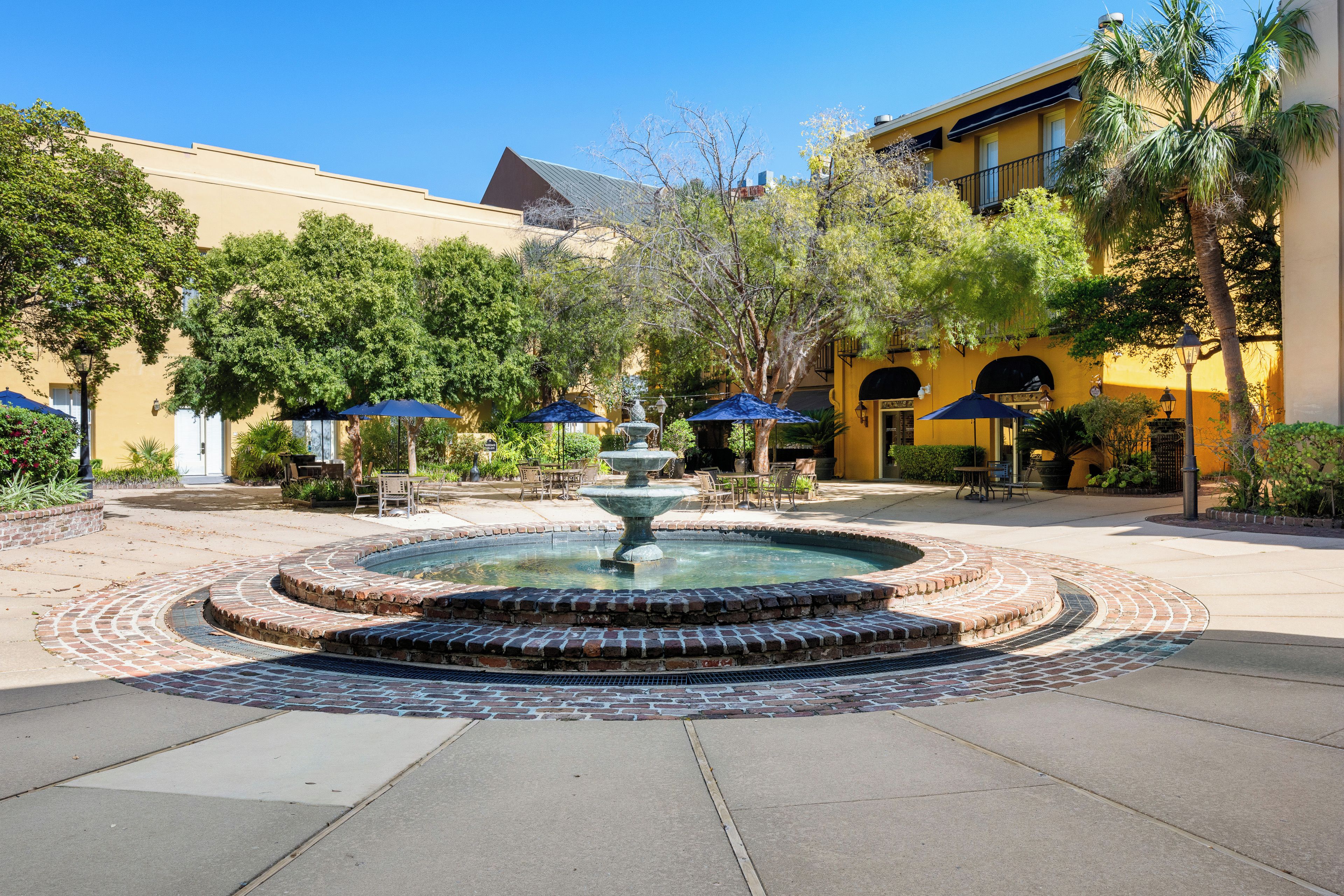 A courtyard with a central fountain, outdoor seating, and a yellow building in the background.