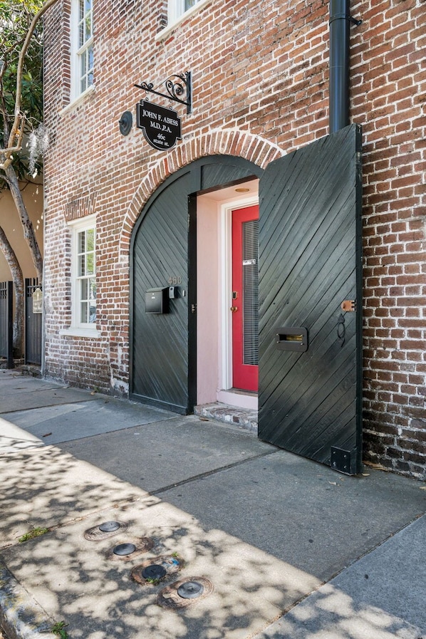 A brick building with a red door and two large black gates. - The Office | Historic District Charleston! (Charleston)