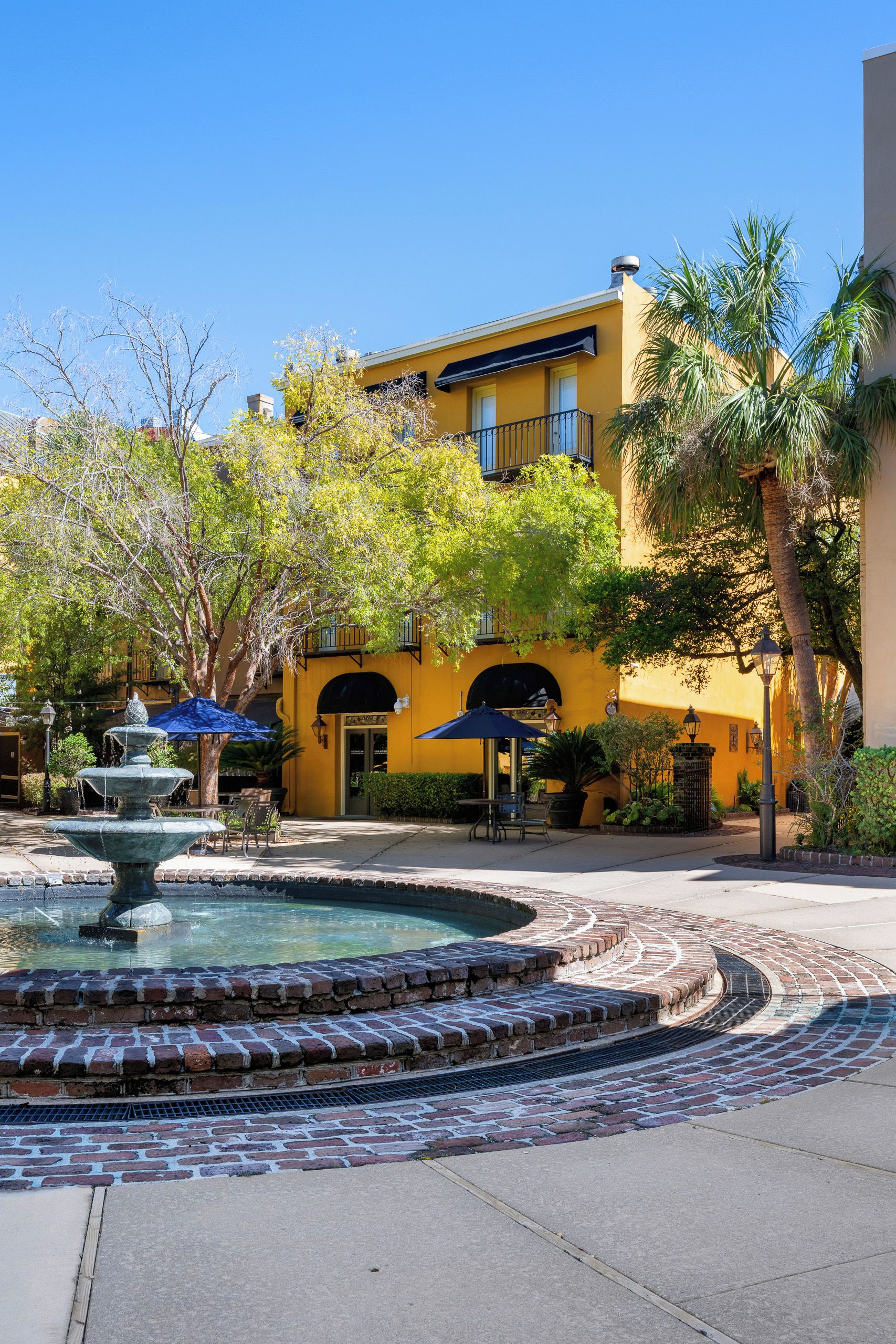 A courtyard with a fountain, outdoor seating, and a yellow building with arched windows.