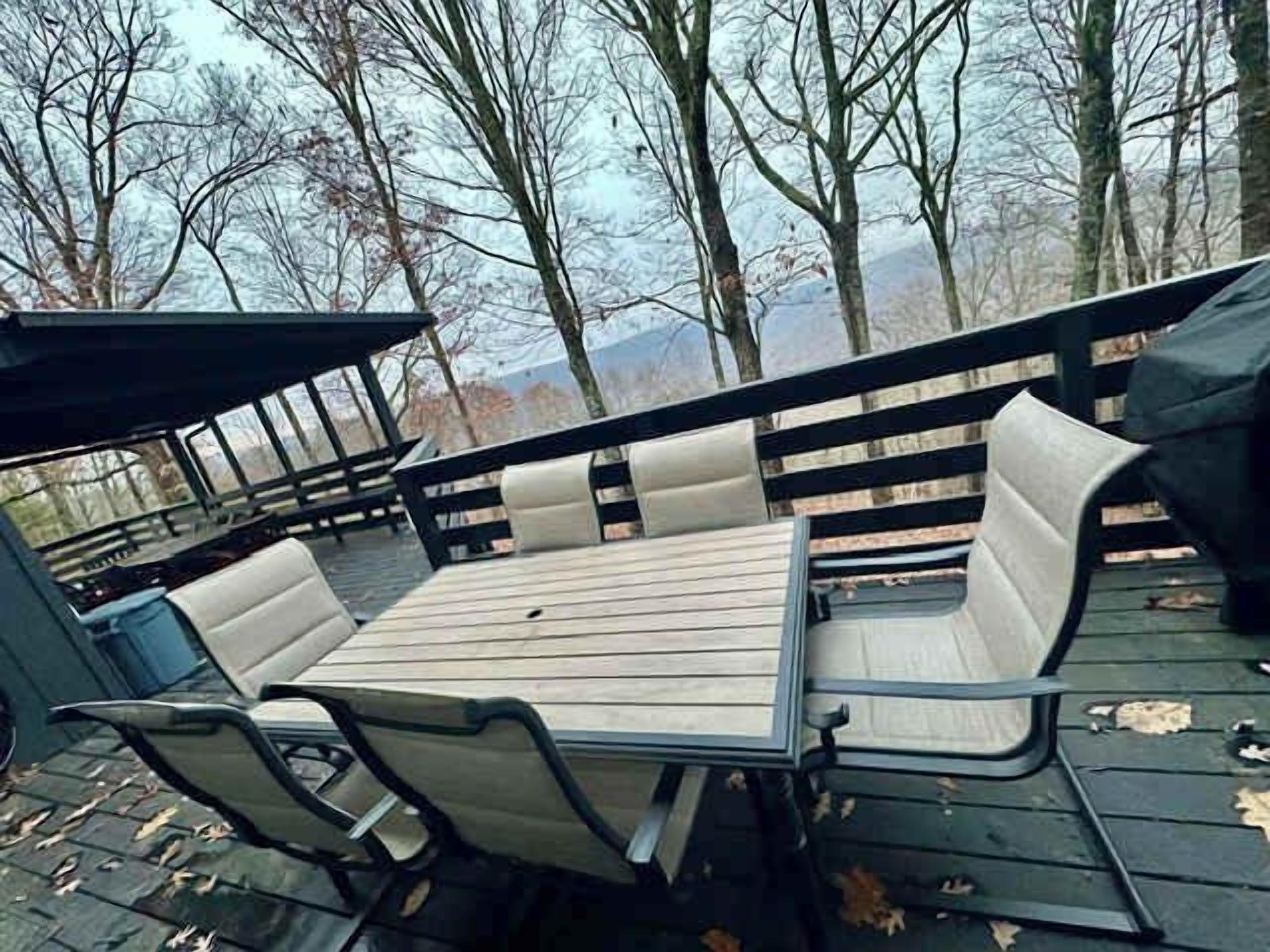 Eine Terrasse im Freien mit Tisch und Stühlen, umgeben von einem Holzzaun und Bäumen.
