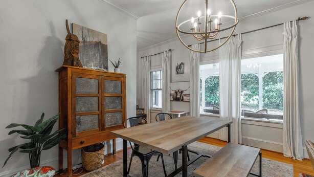 A dining area with a wooden table and benches, a chandelier, and a view of greenery outside.