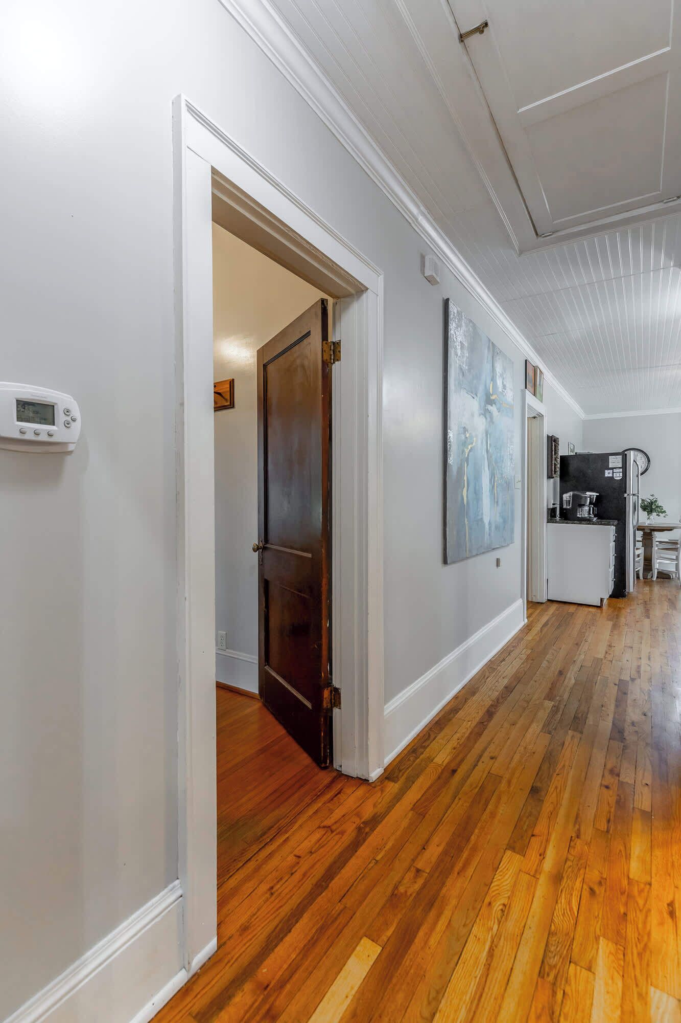 A hallway with wooden flooring, white walls, and a door leading to another room.