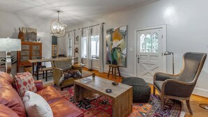 A living room with a sofa, coffee table, chairs, a dining table, and artwork on the walls.