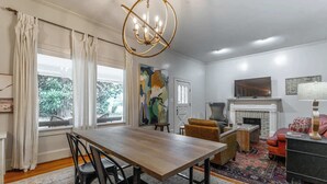A dining area with a wooden table and chairs, a fireplace, a television, and a large window with curtains.