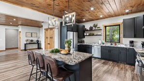 A modern kitchen with dark cabinets, a marble island, and a wooden ceiling. - Priddy Secluded by Avantstay Hot Tub + Expansive Deck + Game Room + Home Theater (Sevierville)