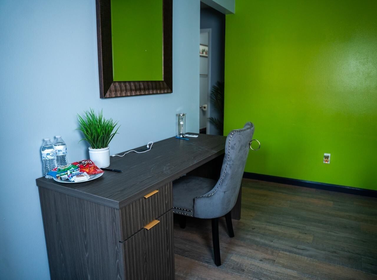 Una habitación con un escritorio de madera oscura, una silla gris, una planta en maceta y una pared verde.