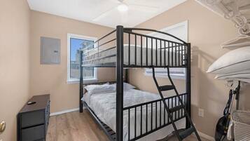 A bunk bed room with a ceiling fan, a small desk, and a vacuum cleaner.
