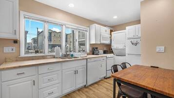 A modern kitchen with white cabinets, a wooden dining table, and a view of neighboring buildings.