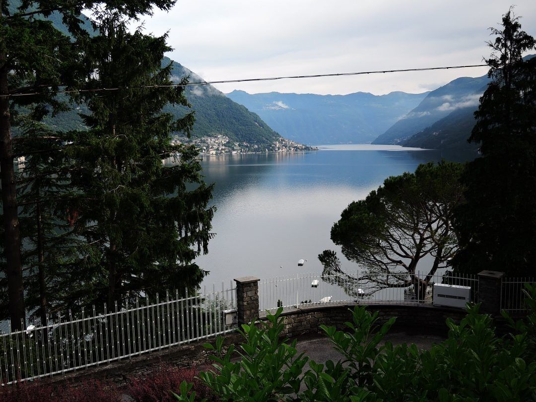 Um lago rodeado por montanhas, uma cerca branca e algumas árvores.