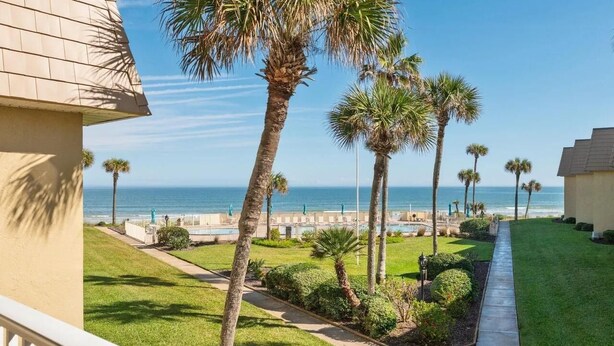 A coastal view with palm trees, a pathway, and a building with a beige facade. - Oceanfront Escape | 2BR Condo | Private Beach Access + Resort Amenities (Saint Augustine)