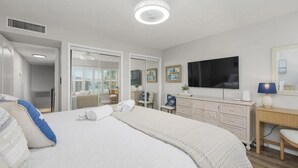 A hotel room with a large bed, a flat-screen TV, a desk, and a wardrobe. - Oceanfront Escape | 2BR Condo | Private Beach Access + Resort Amenities (Saint Augustine)