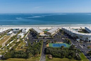 Vista aérea de un hotel costero con vistas a la playa, varias edificaciones y una cancha de tenis.