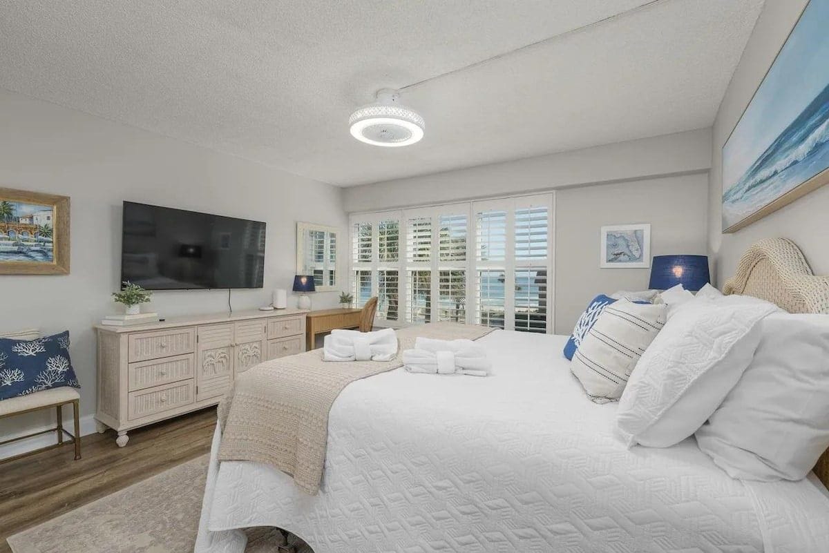 A bedroom with a large bed, a television, a dresser, and a window with blinds.