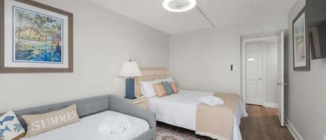 A bedroom with two beds, a nightstand, a lamp, a framed picture, and a door.