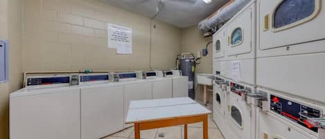 A laundry room with multiple washing machines and dryers, a ceiling fan, and a table.