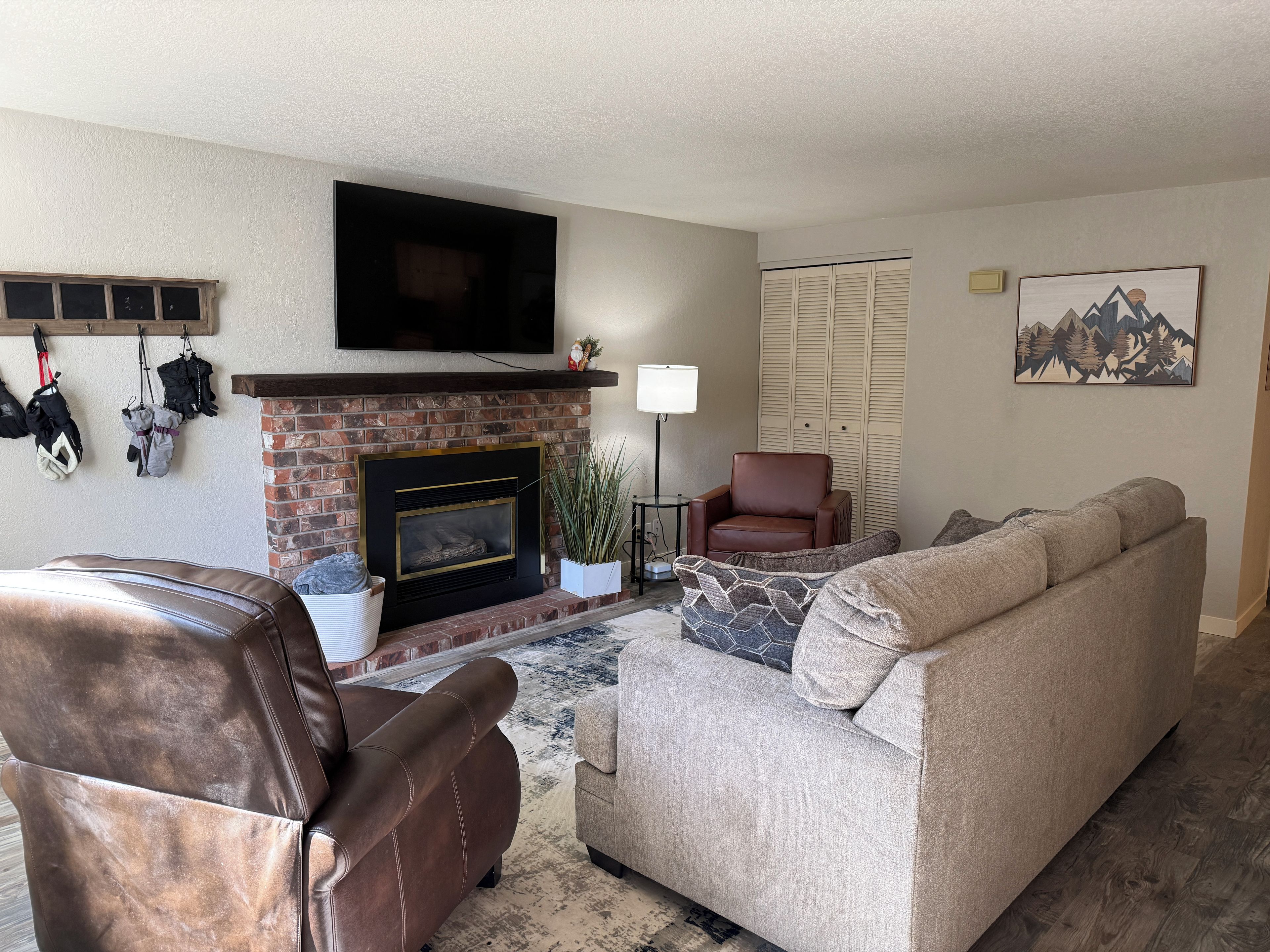 A living room with a fireplace, leather armchair, sofa, and a flat-screen TV mounted above the fireplace.