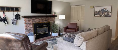 A living room with a fireplace, leather armchair, sofa, and a flat-screen TV mounted above the fireplace.