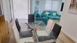 A modern living room with a glass dining table, teal sofas, and a wooden cabinet. - Townhouse with pool in Benicasim 400 m from El Torreon beach (Benicàssim)