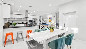 Une cuisine moderne avec des meubles blancs, des appareils en acier inoxydable et un coin repas comprenant une table blanche et des chaises de couleur turquoise.