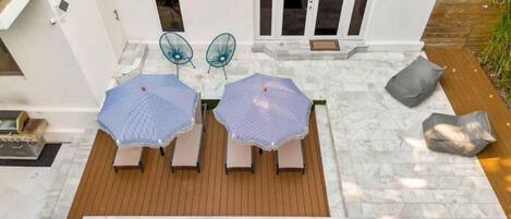 A patio with two lounge chairs and a table, a small pool, and a wooden deck.