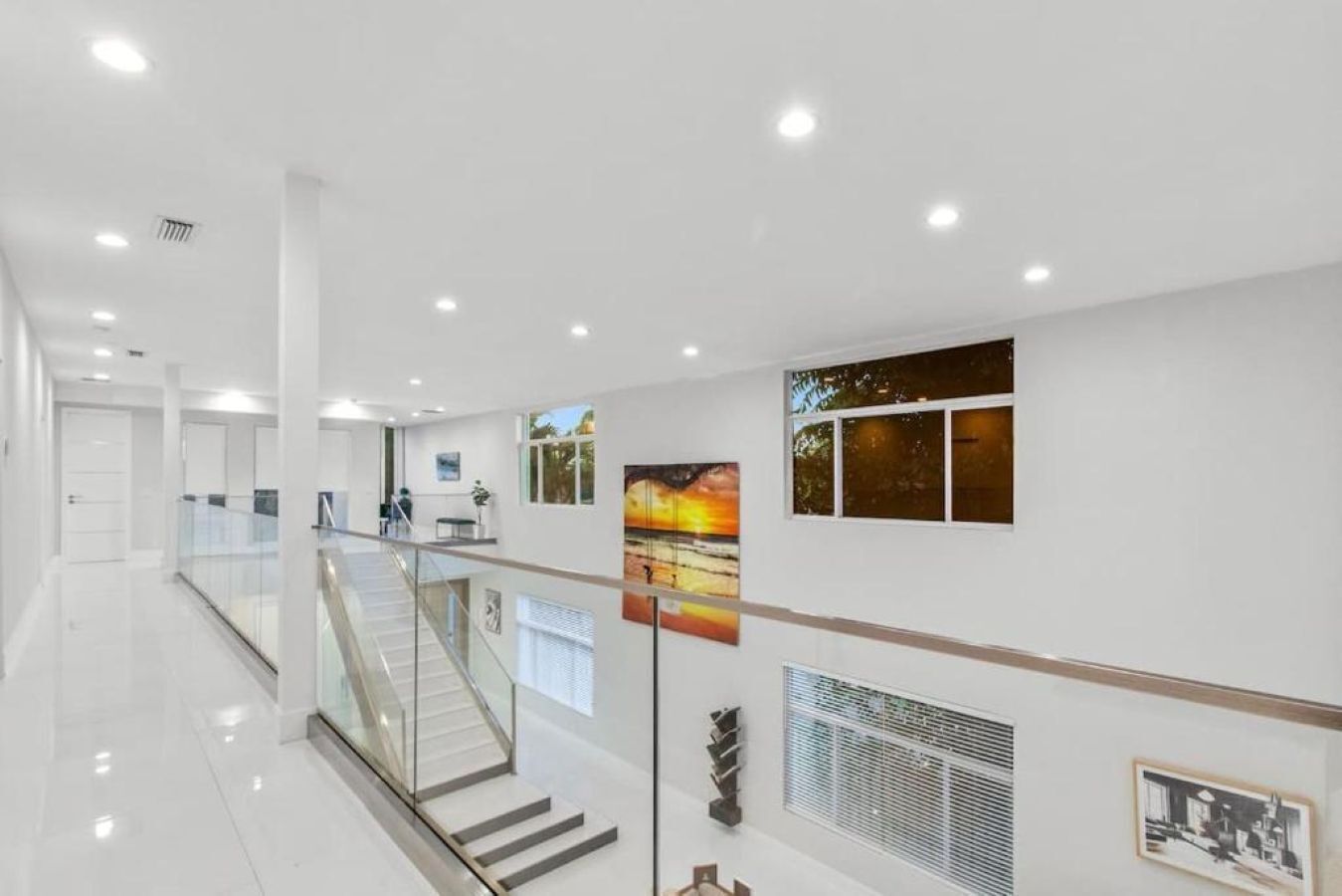 A modern hotel lobby with a glass staircase, a reception desk, and artwork on the walls.