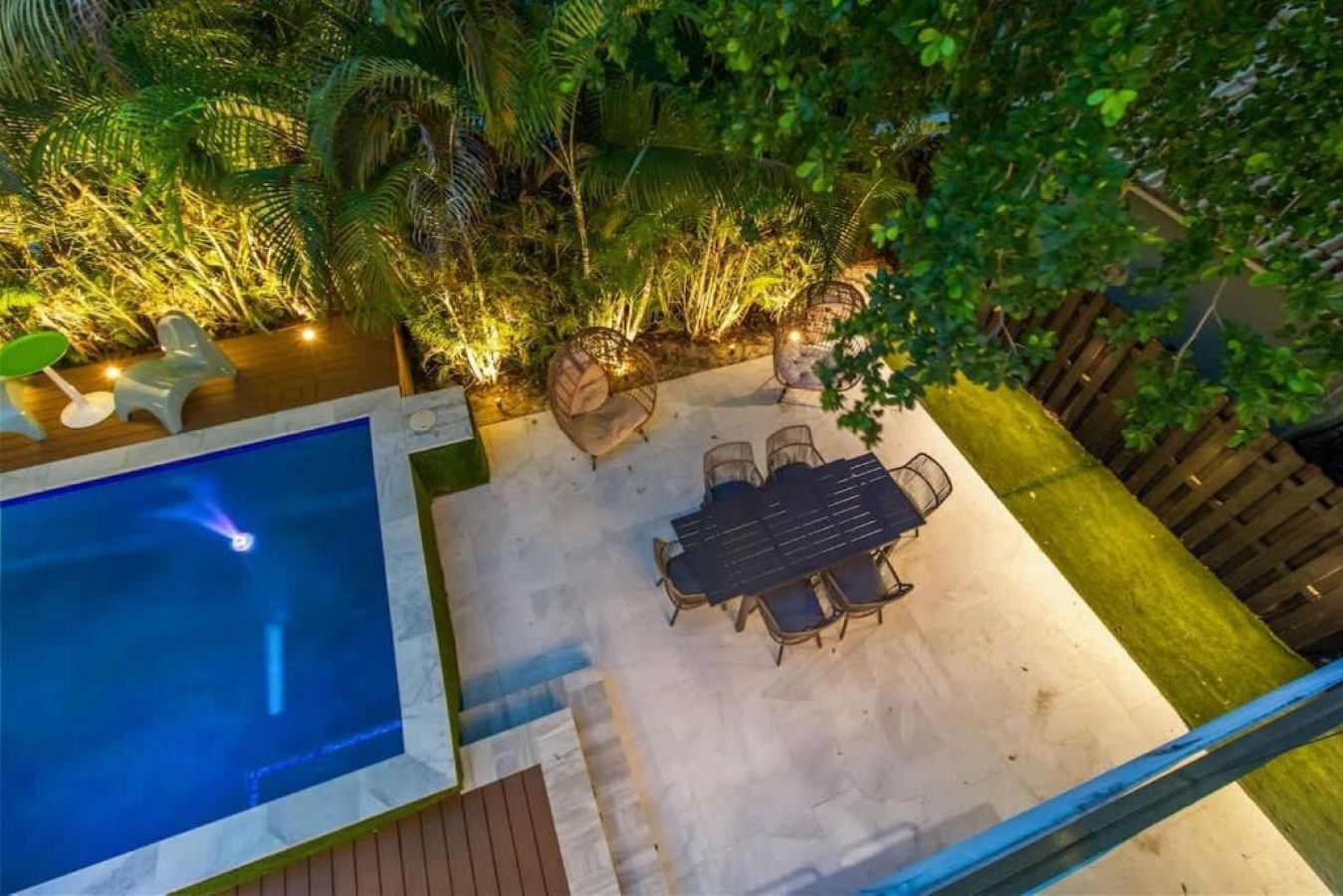 Un área de piscina en la azotea con mesa y sillas, rodeada de abundante vegetación y una terraza de madera.