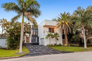 Una casa moderna de dos pisos con un camino de entrada delantero, palmeras y un césped bien cuidado.