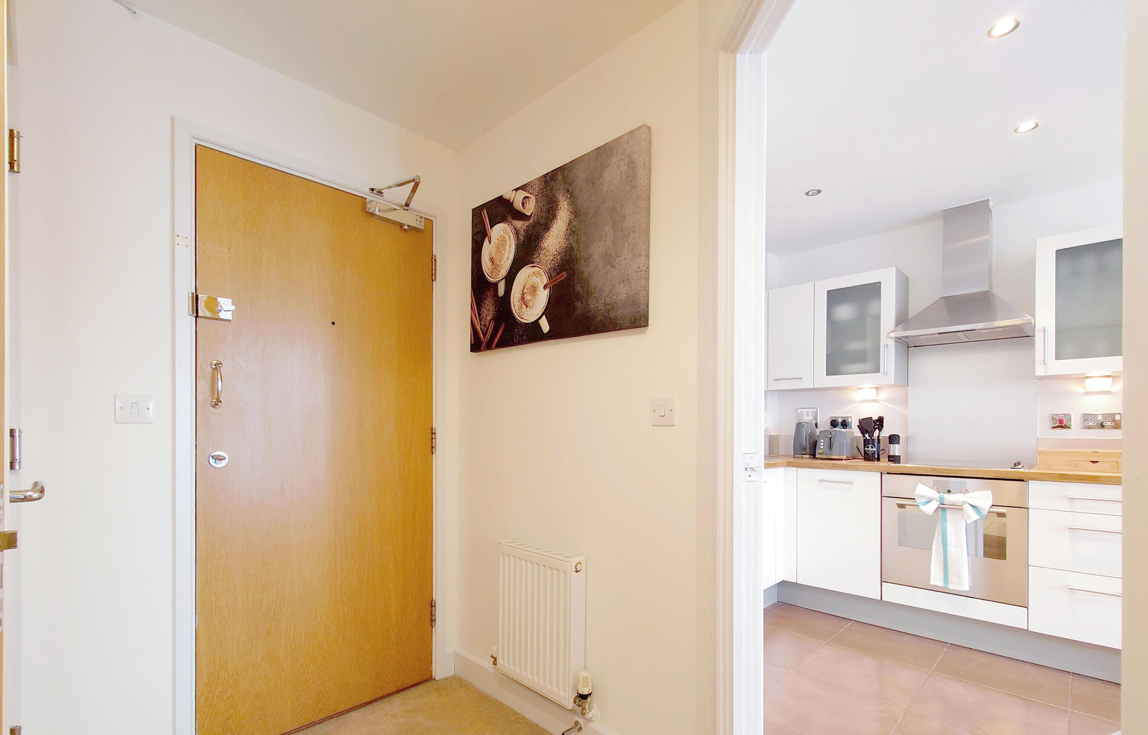 A modern kitchen with white cabinets, a wooden door, and a painting on the wall.