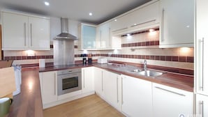 A modern kitchen with white cabinets, a stainless steel range hood, a built-in oven, a double sink, and a wooden countertop. - Capital Stay - Two Bed Apartments Near Lcy (London)