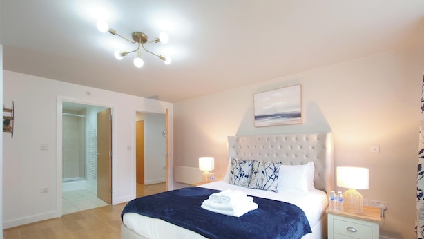 A bedroom with a bed, bedside lamps, a ceiling light, a painting, and a view of a hallway. - Capital Stay - Two Bed Apartments Near Lcy (London)