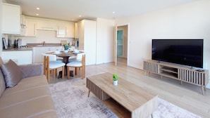 A modern living room with a sofa, coffee table, TV, and a dining area with chairs and a table. - Capital Stay - Two Bed Apartments Near Lcy (London)