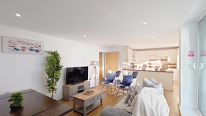A modern living room with a flat-screen TV, a coffee table, and two rocking chairs. - Capital Stay - Two Bed Apartments Near Lcy (London)
