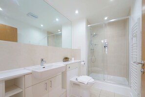 A modern bathroom with a glass-enclosed shower, a white sink, and a large mirror. - Capital Stay - Two Bed Apartments Near Lcy (London)