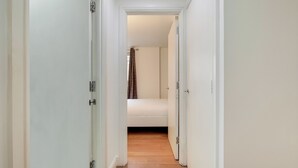 Un pasillo estrecho con puertas blancas que dan a un dormitorio con cama y cortina.