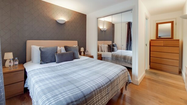 Una habitación de hotel moderna con una cama grande, mesitas de noche, un espejo y un armario.