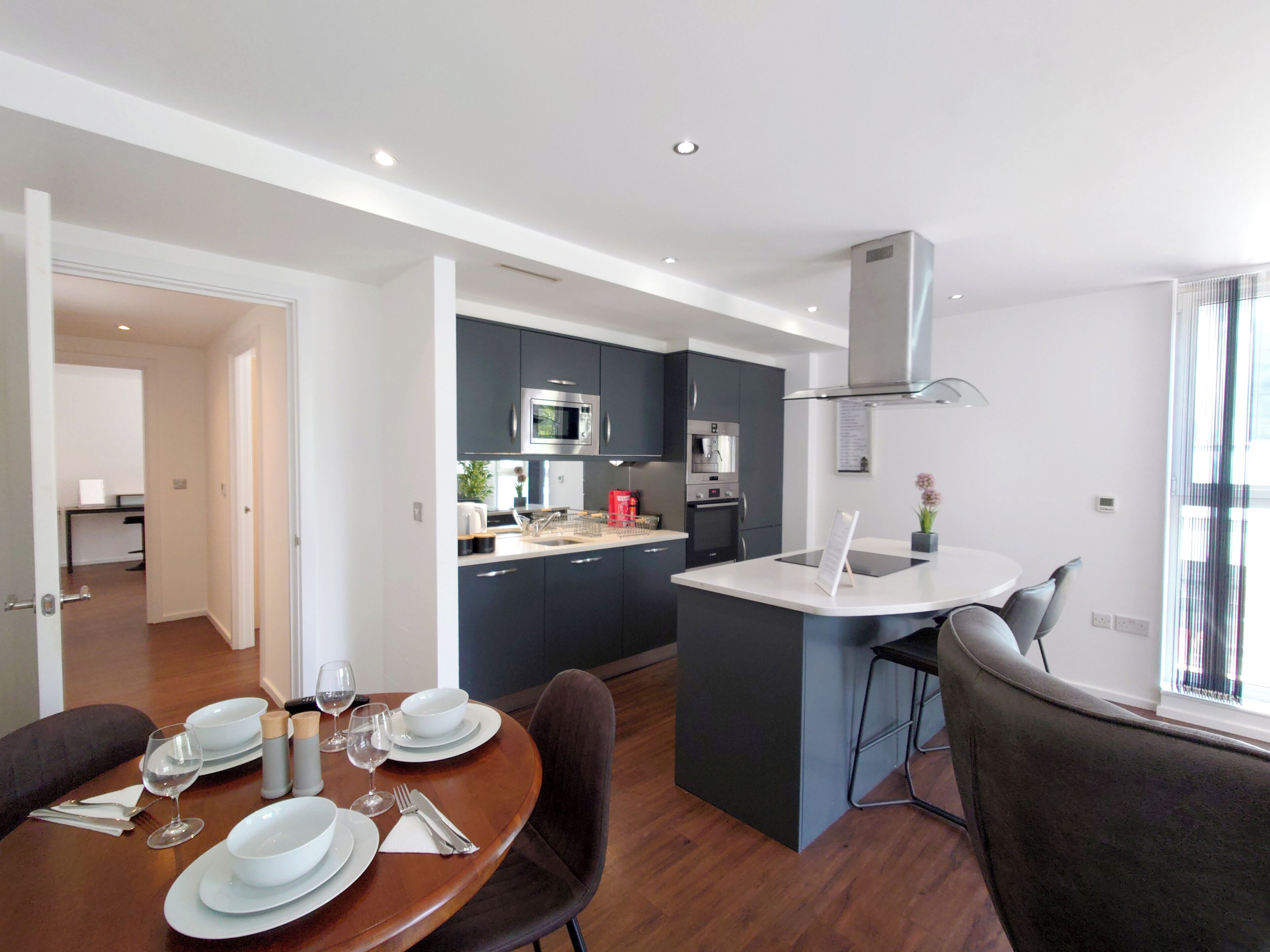 A modern kitchen with dark cabinets, a central island, and a dining area with a wooden table set for four.