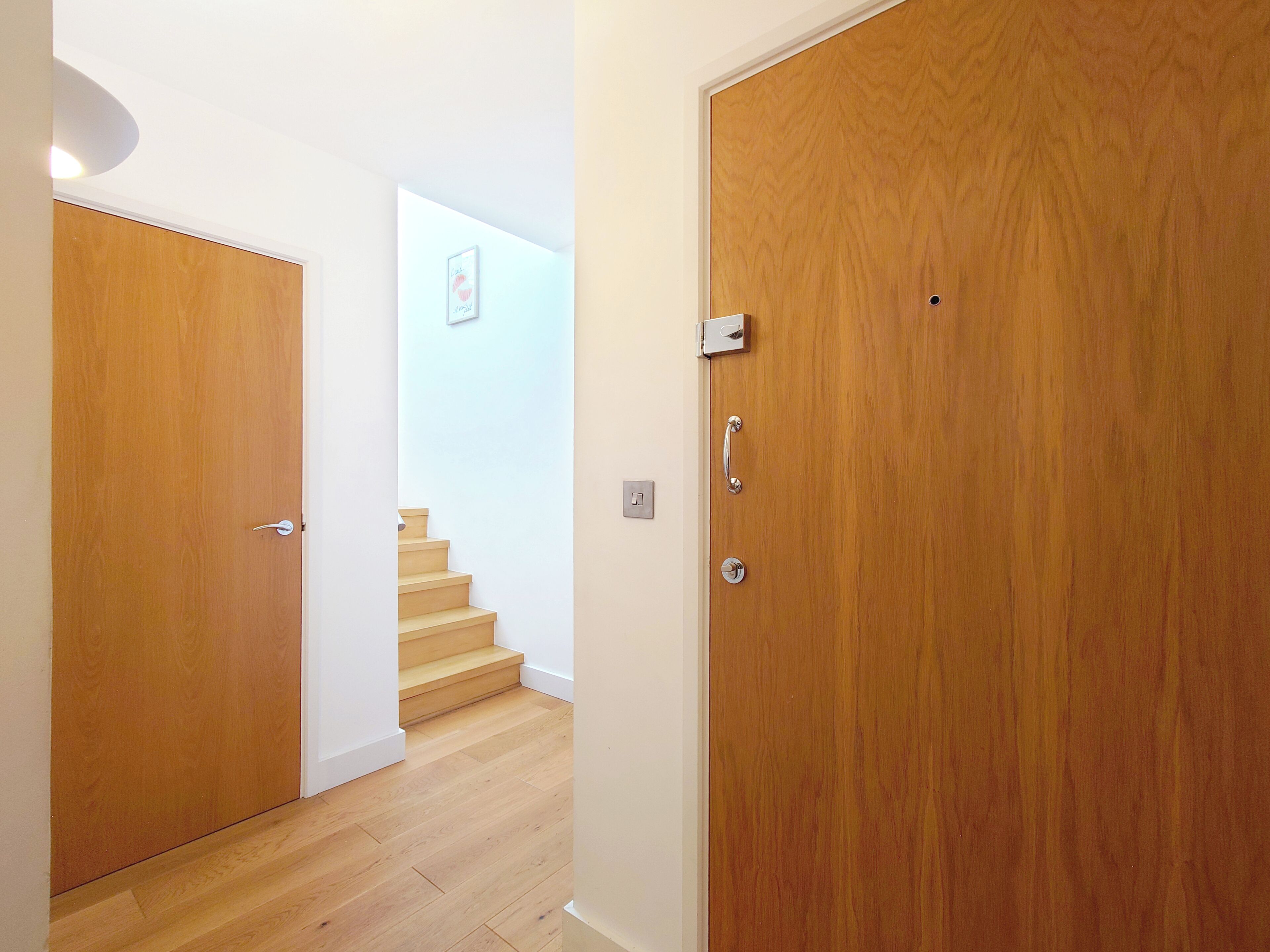 A wooden door with a handle and a lock, leading to a staircase with wooden steps and a white wall.