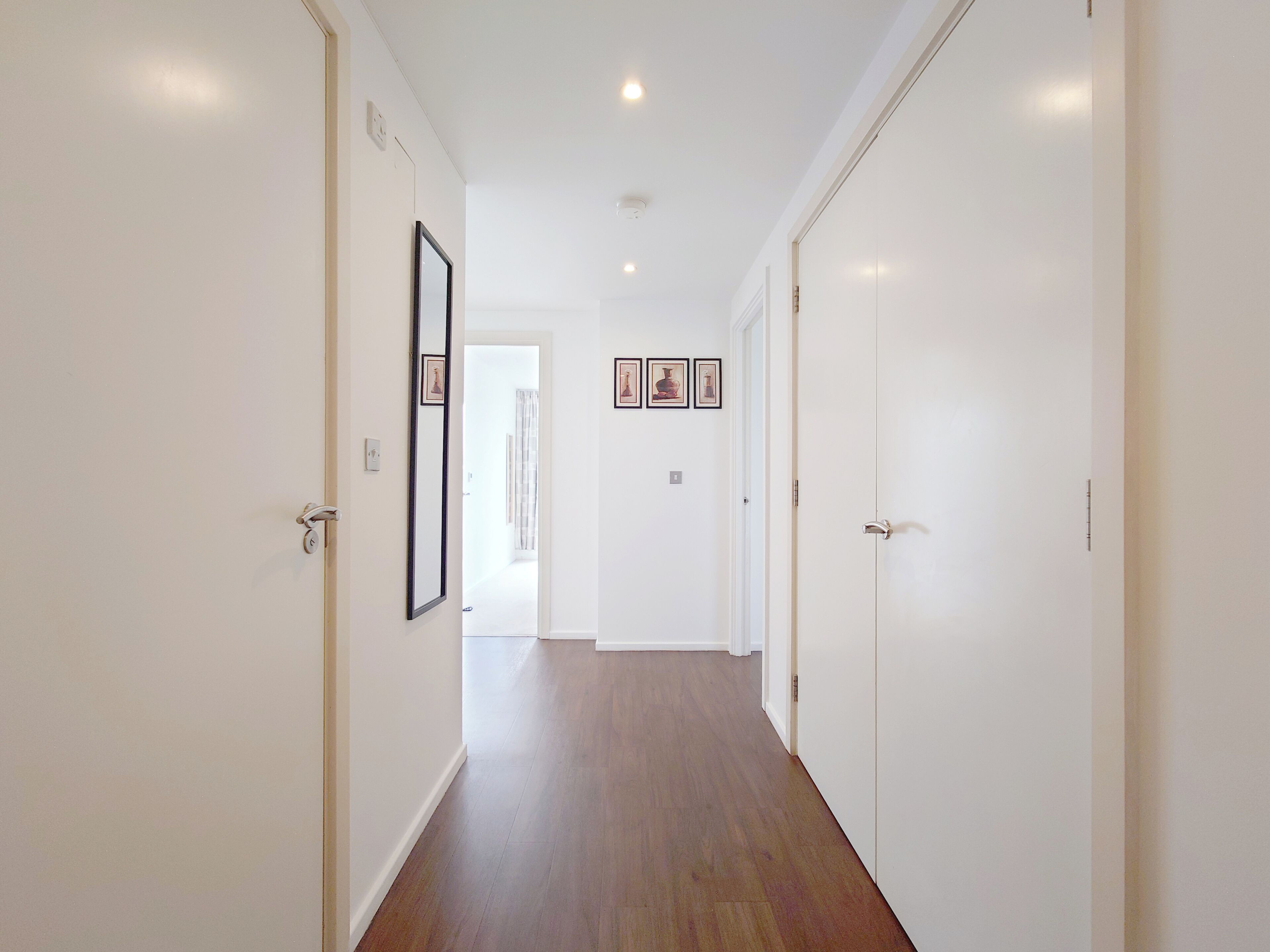 Un couloir aux murs blancs, au sol en bois et dont les deux côtés sont bordés de portes.