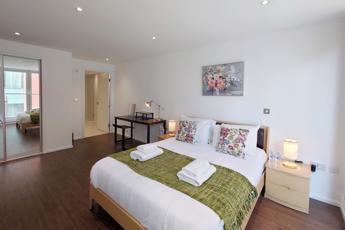 A modern hotel room with a bed, bedside tables, a desk, and a mirror.