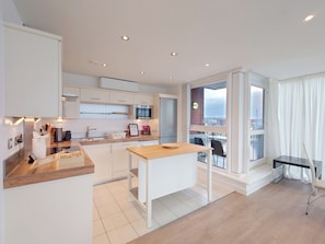 A modern kitchen with white cabinetry, a wooden countertop, and a view of the city through large windows.