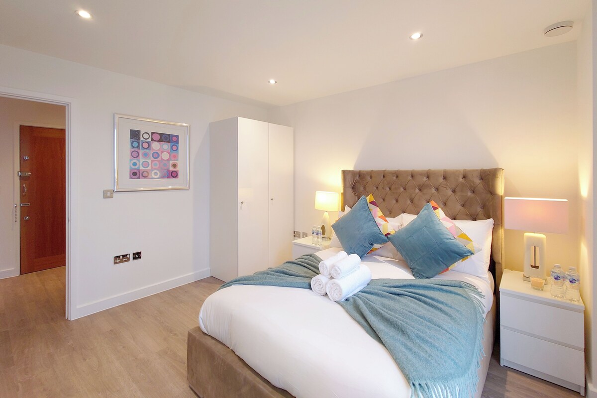 A hotel room with a bed, bedside tables, a nightstand, a door, and a framed picture on the wall.