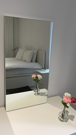 Ein Schlafzimmer mit Bett, Nachttisch und einem Spiegel, der den Raum reflektiert.
