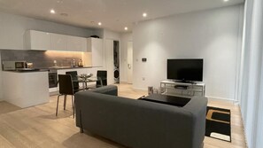 Ein modernes Wohnzimmer mit grauem Sofa, einem Flachbildfernseher und einem Essbereich mit Tisch und Stühlen.