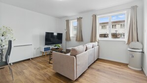A modern living room with a sofa, TV, and a window with curtains. - Two Bed Serviced Apartment (London)