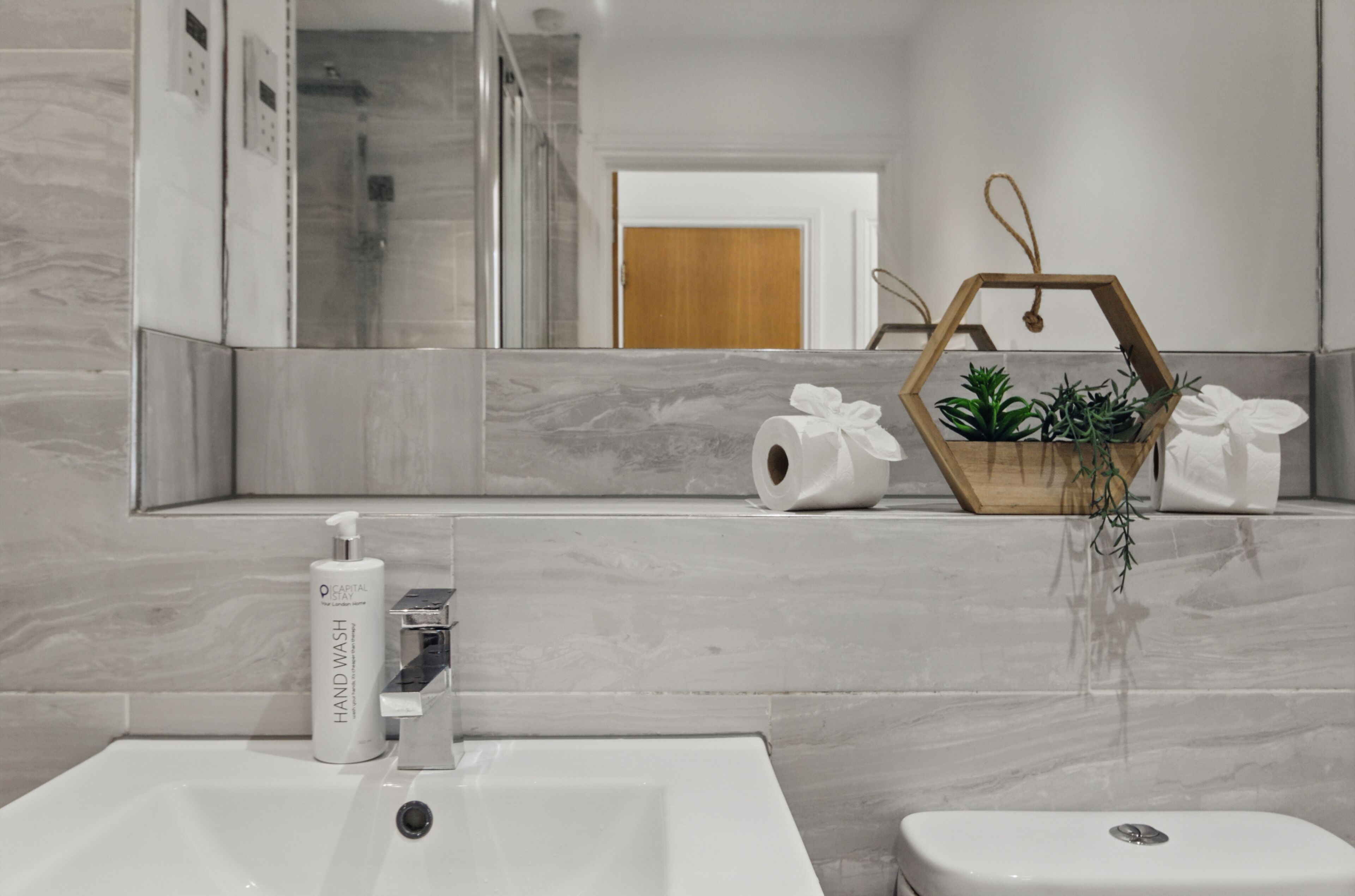 Une salle de bain avec un lavabo en marbre, des toilettes, un miroir, une douche et un bac à fleurs en bois contenant des plantes.