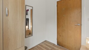 A hallway with a wooden door, a mirror, and a small table with a lamp. - Two Bed Serviced Apartment (London)