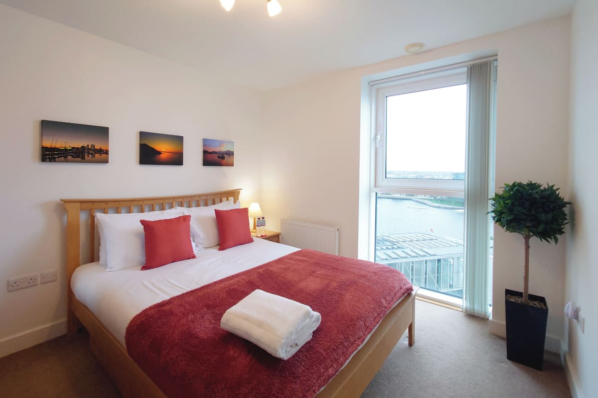 A hotel room with a bed, a window with a view, and a plant.